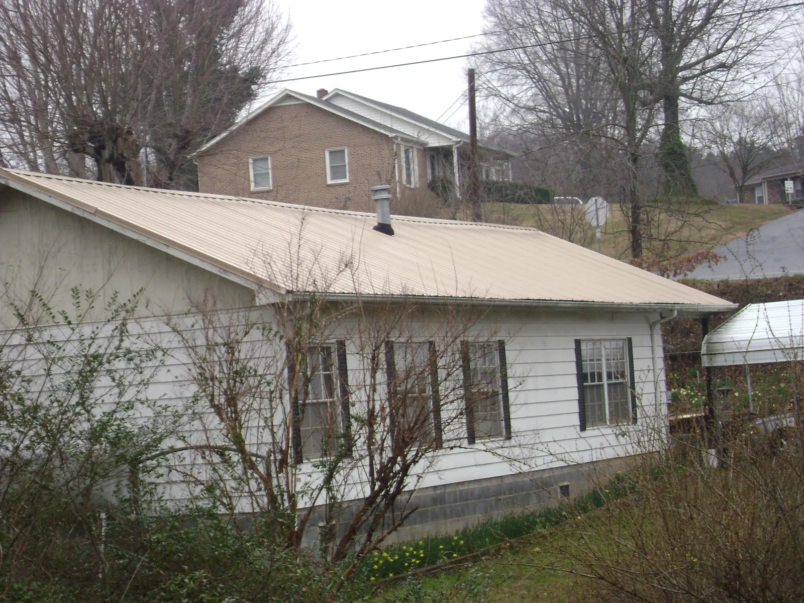 Tan metal roof on a white sided house set into a hillside — Commercial Roofing by Roofing Brothers in Pomona